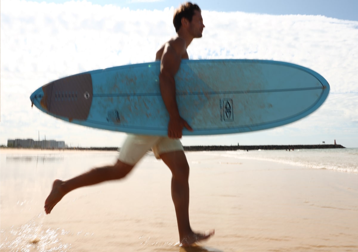 young man running with surf board on vilamoura beach